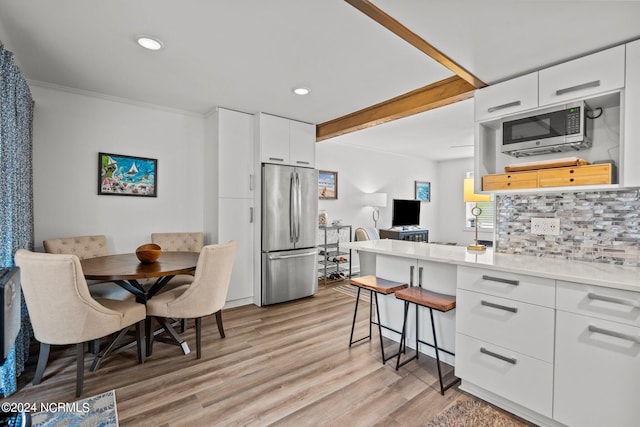 kitchen with stainless steel appliances, a breakfast bar, backsplash, white cabinetry, and light hardwood / wood-style flooring