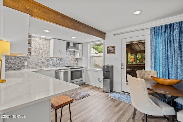 kitchen featuring light wood-type flooring, stainless steel dishwasher, decorative backsplash, wall chimney range hood, and stove