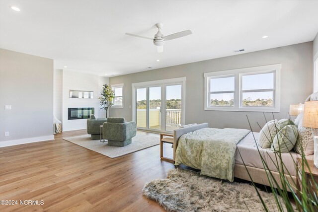 bedroom featuring access to exterior, a fireplace, light hardwood / wood-style floors, and ceiling fan