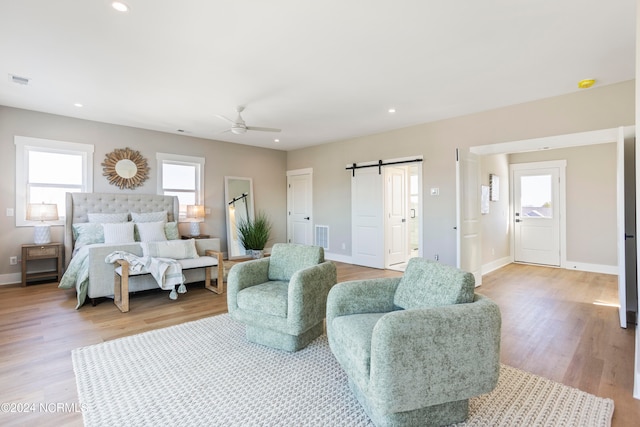 bedroom featuring a barn door, light wood-type flooring, and ceiling fan