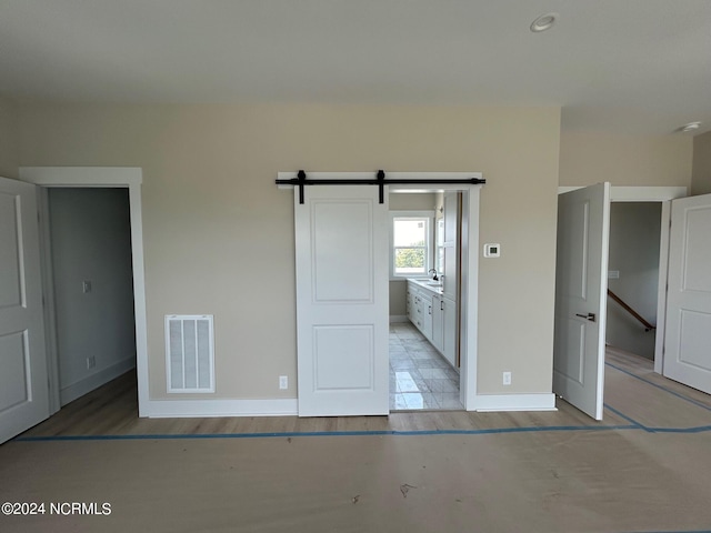 unfurnished bedroom featuring ensuite bathroom, light wood-type flooring, and a barn door