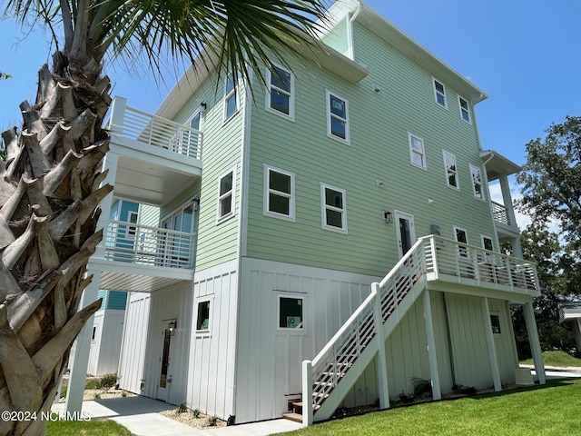 back of house featuring board and batten siding, a lawn, and stairway