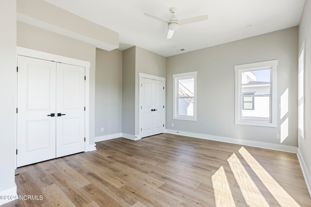 unfurnished bedroom with light hardwood / wood-style flooring, two closets, and ceiling fan