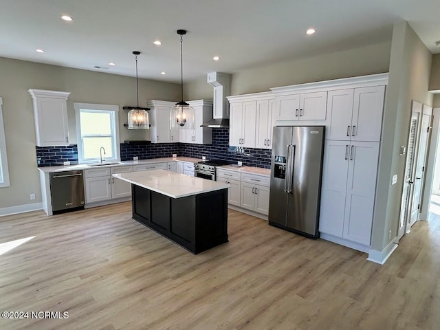 kitchen with wall chimney range hood, white cabinets, a kitchen island, light hardwood / wood-style flooring, and stainless steel appliances