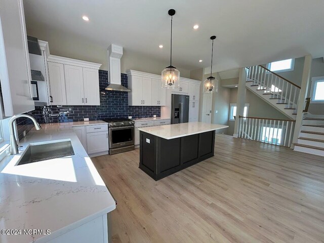 kitchen featuring wall chimney range hood, sink, a kitchen island, white cabinetry, and stainless steel appliances