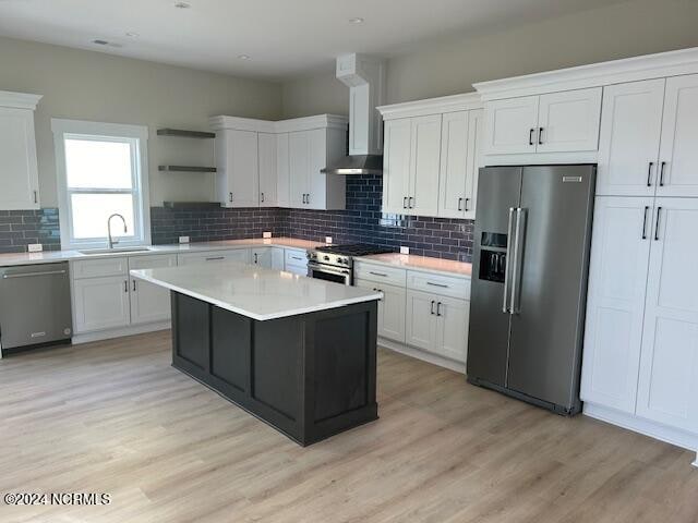 kitchen with wall chimney range hood, sink, a center island, stainless steel appliances, and white cabinets