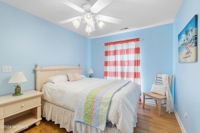 bedroom with a ceiling fan, visible vents, baseboards, and wood finished floors