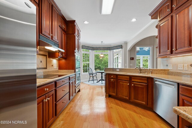 kitchen with appliances with stainless steel finishes, light hardwood / wood-style floors, ornamental molding, sink, and decorative backsplash