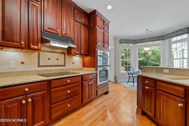 kitchen featuring black electric stovetop, stainless steel double oven, decorative light fixtures, light stone counters, and light hardwood / wood-style floors