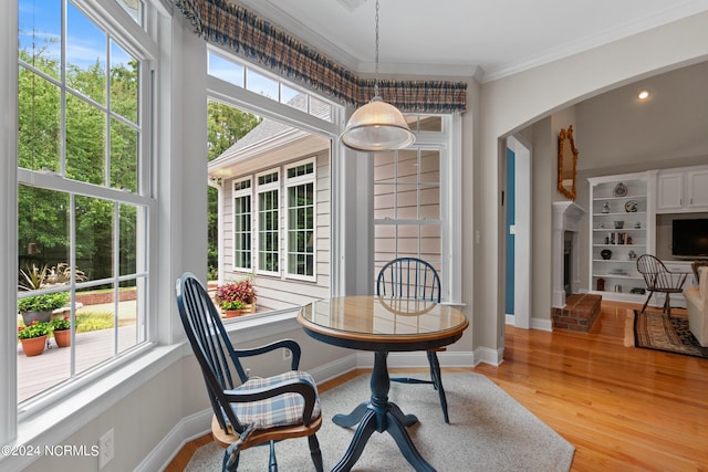 dining room with arched walkways, light wood finished floors, baseboards, and crown molding