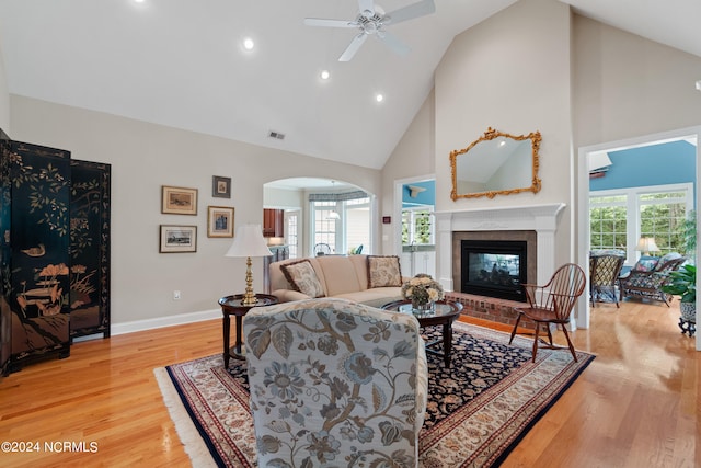 living area with baseboards, arched walkways, light wood-type flooring, a fireplace, and high vaulted ceiling