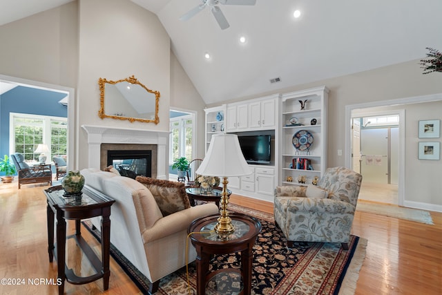 living room featuring high vaulted ceiling, light wood-style flooring, a glass covered fireplace, and visible vents