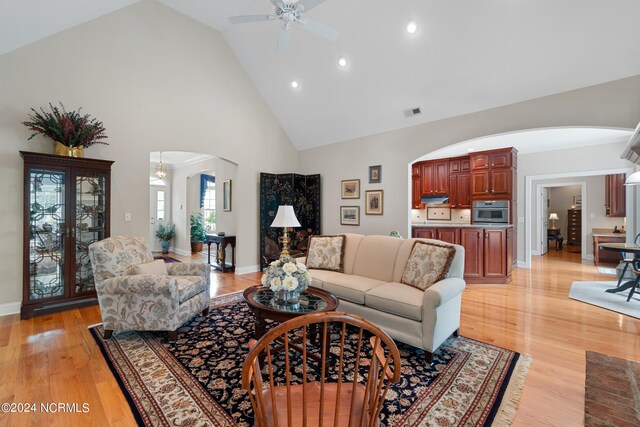 living room with high vaulted ceiling, ceiling fan, and light hardwood / wood-style flooring