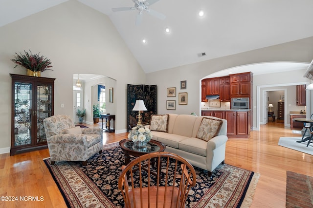 living room featuring arched walkways, visible vents, high vaulted ceiling, light wood-type flooring, and baseboards