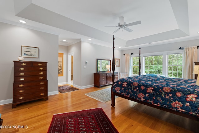 bedroom with crown molding, light hardwood / wood-style flooring, a tray ceiling, and ceiling fan