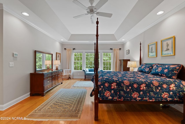 bedroom with ceiling fan, ornamental molding, light wood-type flooring, and a tray ceiling