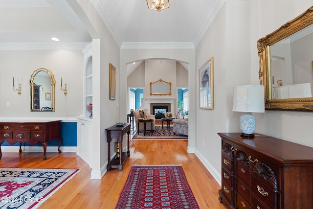 entrance foyer with light wood-style floors, a fireplace, ornamental molding, and baseboards