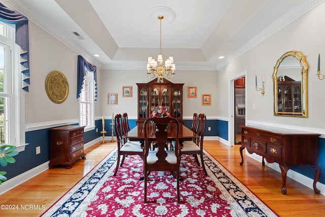 dining space with a chandelier, a tray ceiling, plenty of natural light, and light wood finished floors