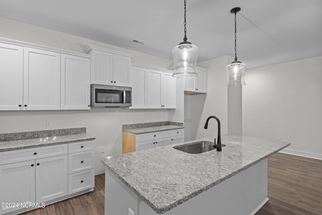 kitchen with white cabinets, dark wood-type flooring, pendant lighting, an island with sink, and sink