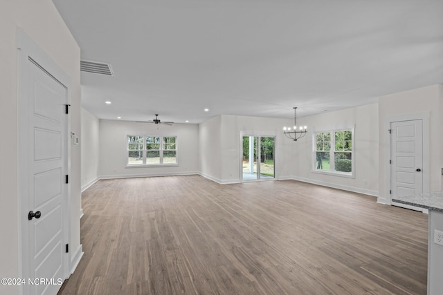 unfurnished living room with ceiling fan with notable chandelier, hardwood / wood-style flooring, and a wealth of natural light