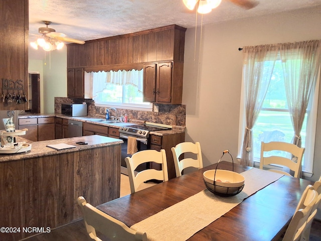 kitchen featuring a textured ceiling, stainless steel appliances, a sink, a ceiling fan, and backsplash