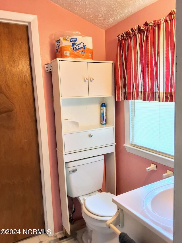 half bathroom with a sink, a textured ceiling, and toilet