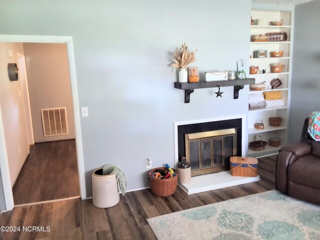 living room featuring a glass covered fireplace, visible vents, and wood finished floors