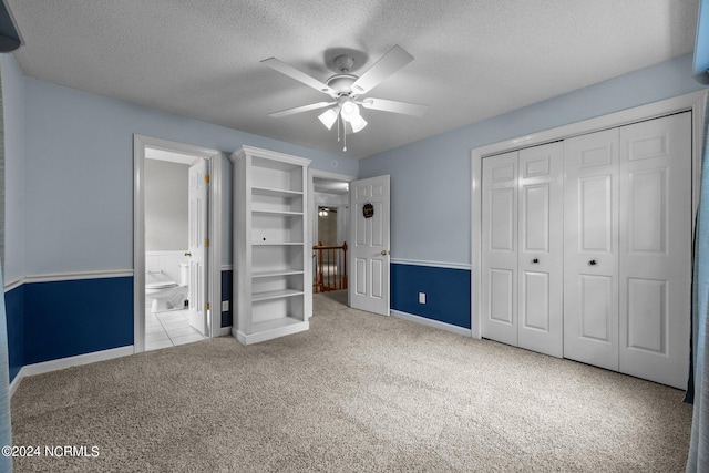 unfurnished bedroom with ceiling fan, light colored carpet, a closet, ensuite bath, and a textured ceiling