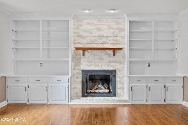 unfurnished living room with a fireplace, light hardwood / wood-style flooring, ornamental molding, and brick wall