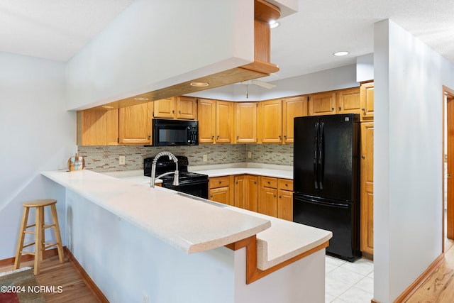 kitchen with black appliances, kitchen peninsula, light hardwood / wood-style flooring, and a kitchen bar