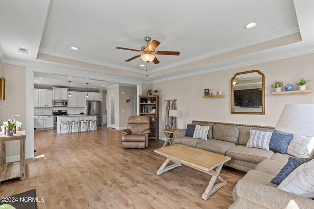 living room featuring light wood-type flooring, a tray ceiling, ornamental molding, and ceiling fan