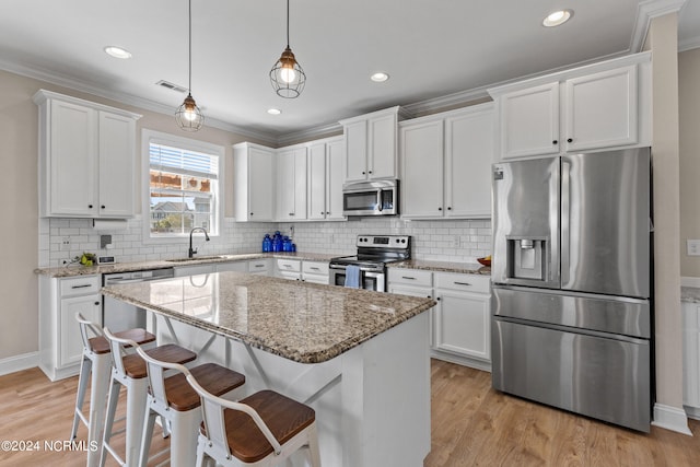 kitchen featuring a kitchen island, decorative light fixtures, light hardwood / wood-style floors, stainless steel appliances, and white cabinets