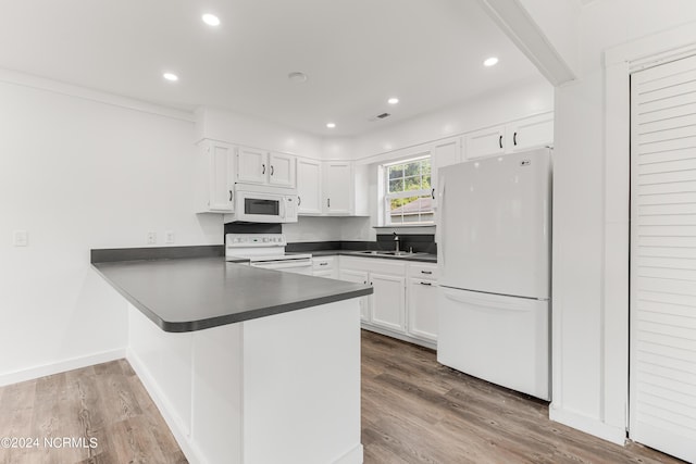 kitchen with dark countertops, white cabinets, wood finished floors, white appliances, and a peninsula