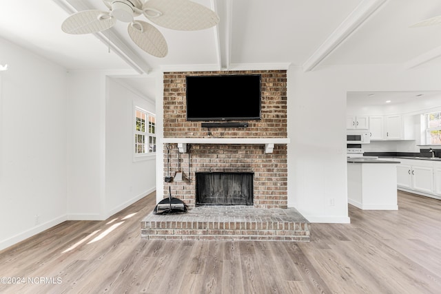 living room featuring light wood-style floors, a fireplace, baseboards, and beamed ceiling