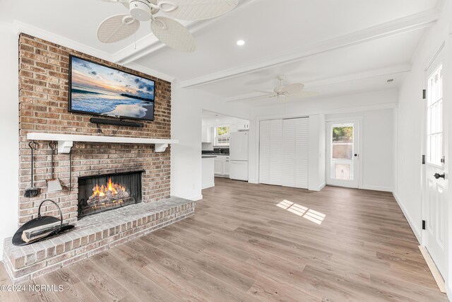 unfurnished living room featuring light hardwood / wood-style floors, a brick fireplace, ceiling fan, and beamed ceiling