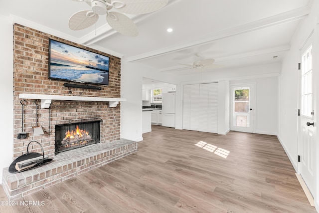 unfurnished living room featuring a ceiling fan, a brick fireplace, beamed ceiling, and light wood finished floors