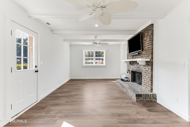 unfurnished living room with ceiling fan, a fireplace, beam ceiling, and wood finished floors