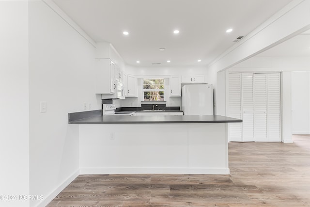 kitchen with a peninsula, white appliances, a sink, white cabinets, and dark countertops