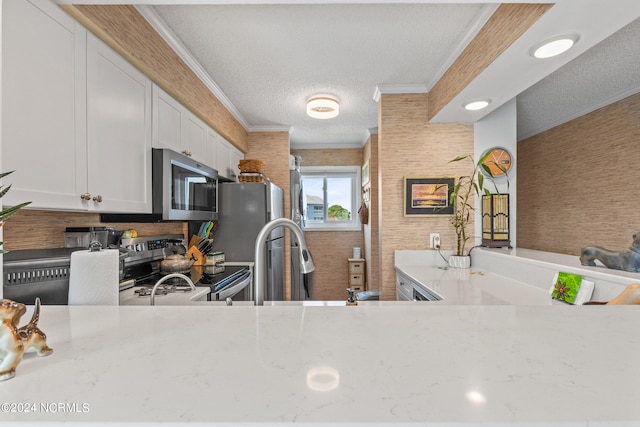 kitchen with a textured ceiling, light stone countertops, stainless steel appliances, and white cabinets