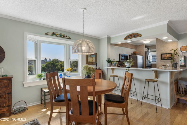 dining room featuring ornamental molding, a textured ceiling, and light hardwood / wood-style flooring