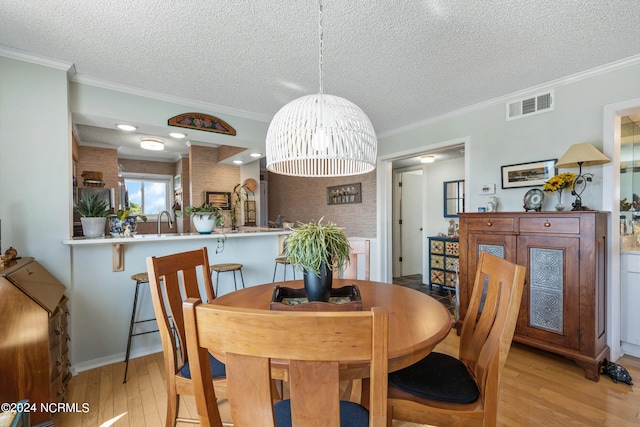 dining space featuring ornamental molding, a textured ceiling, sink, and light hardwood / wood-style floors