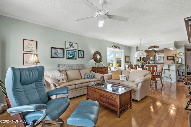 living room with light wood-type flooring, ceiling fan, a textured ceiling, and ornamental molding