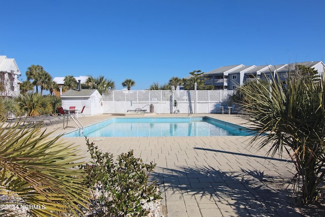 pool with a storage shed, fence, an outdoor structure, and a patio