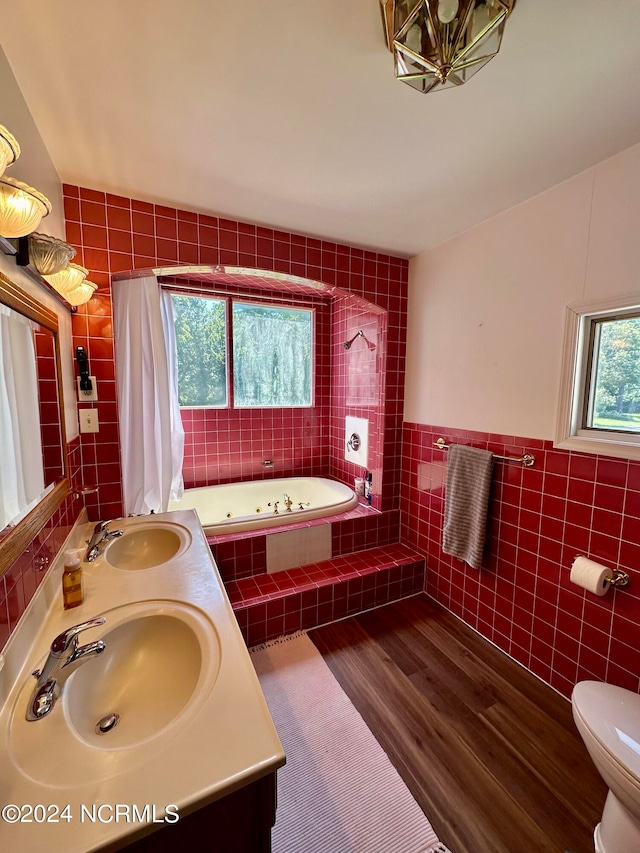 bathroom featuring hardwood / wood-style floors, vanity, a relaxing tiled tub, toilet, and tile walls