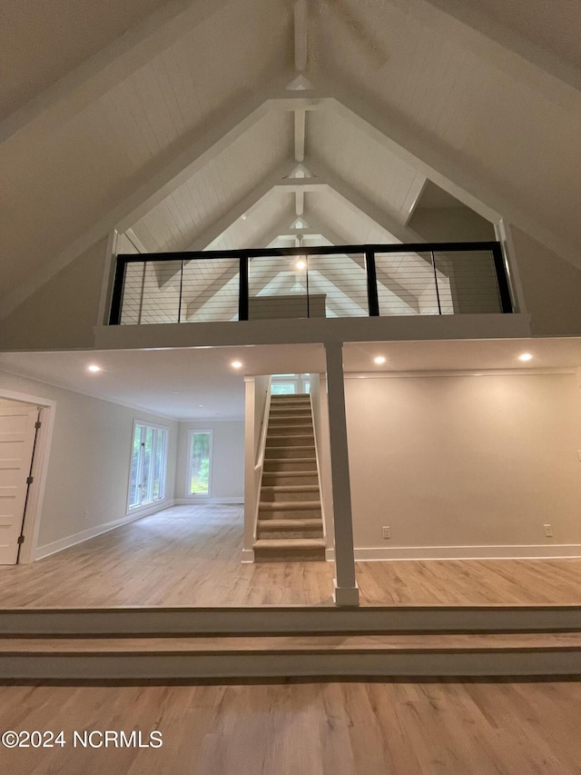 unfurnished living room with stairway, baseboards, high vaulted ceiling, and wood finished floors