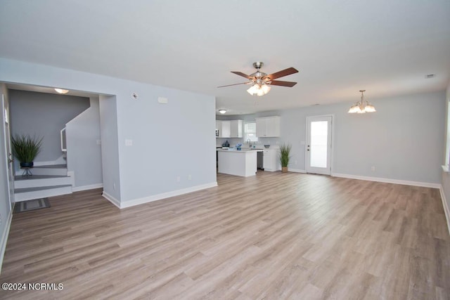 unfurnished living room with ceiling fan with notable chandelier and light hardwood / wood-style flooring