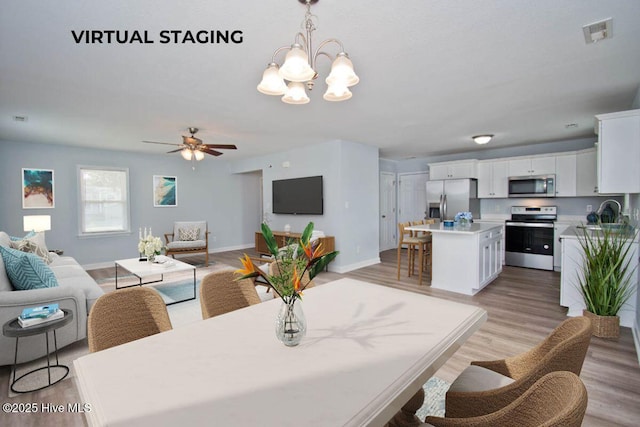 dining area featuring ceiling fan with notable chandelier, light wood-type flooring, and sink