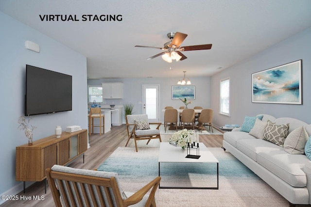 living room with ceiling fan with notable chandelier, light hardwood / wood-style floors, and a healthy amount of sunlight