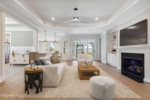 5037 Saltgrass Cv, Leland, NC 28451 - living area with light wood-type flooring, a raised ceiling, a glass covered fireplace, ornamental molding, and recessed lighting