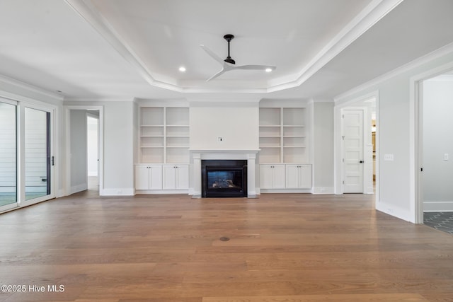 5037 Saltgrass Cv, Leland, NC 28451 - unfurnished living room featuring a tray ceiling, a ceiling fan, built in shelves, baseboards, and crown molding